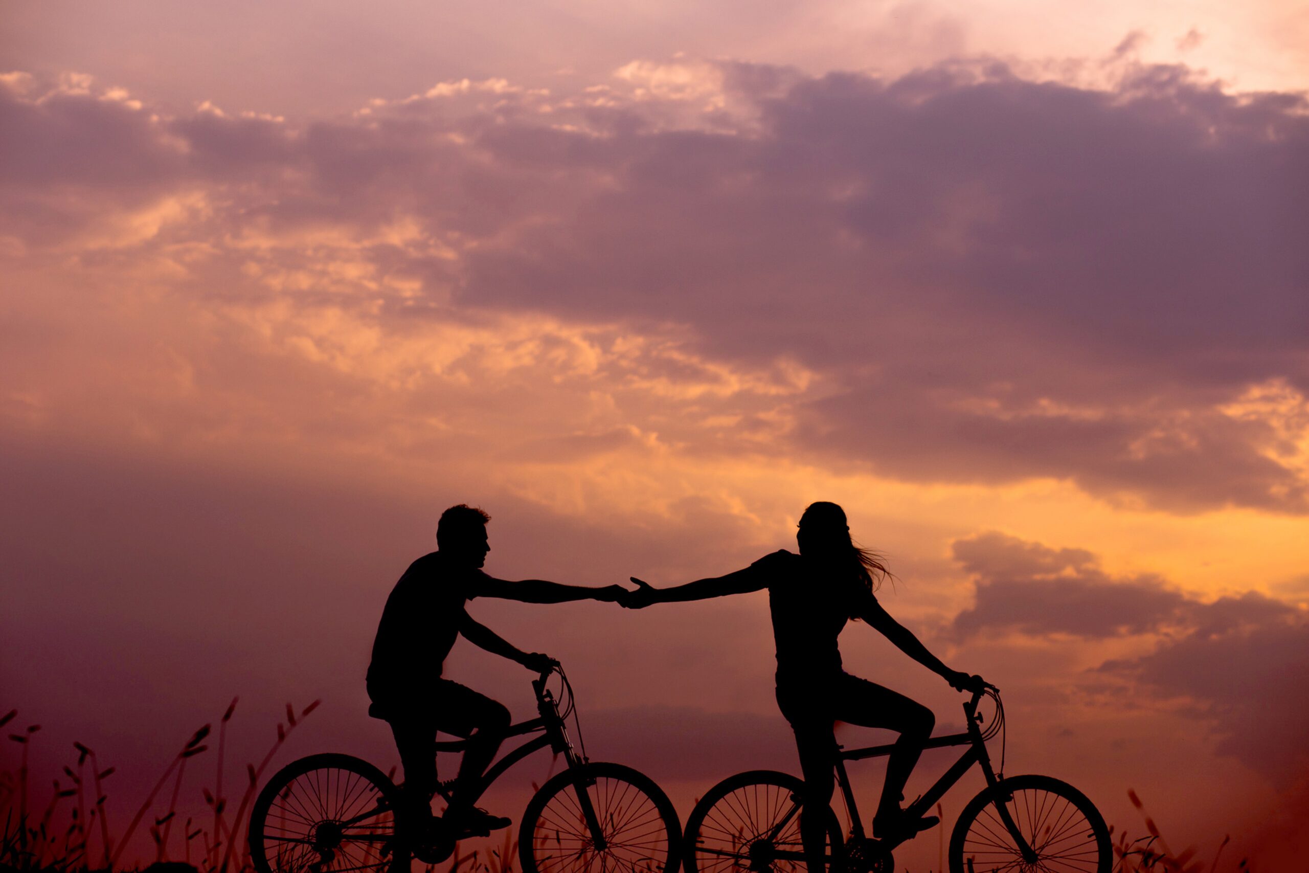 Couple holding hands while bicyling in front of a sunset