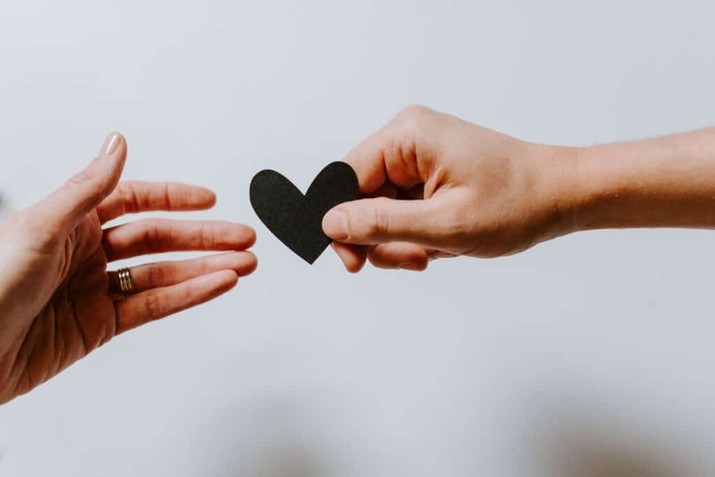 person handing black paper heart to an outstretched hand