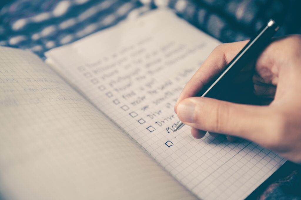 Person writing list with black pen on grid paper notebook