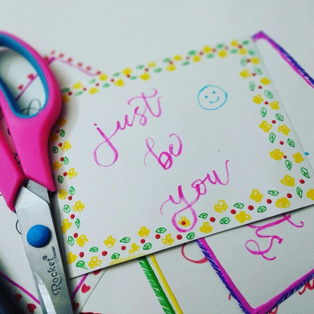 Pink scissors on hand-drawn card reading "just be you"